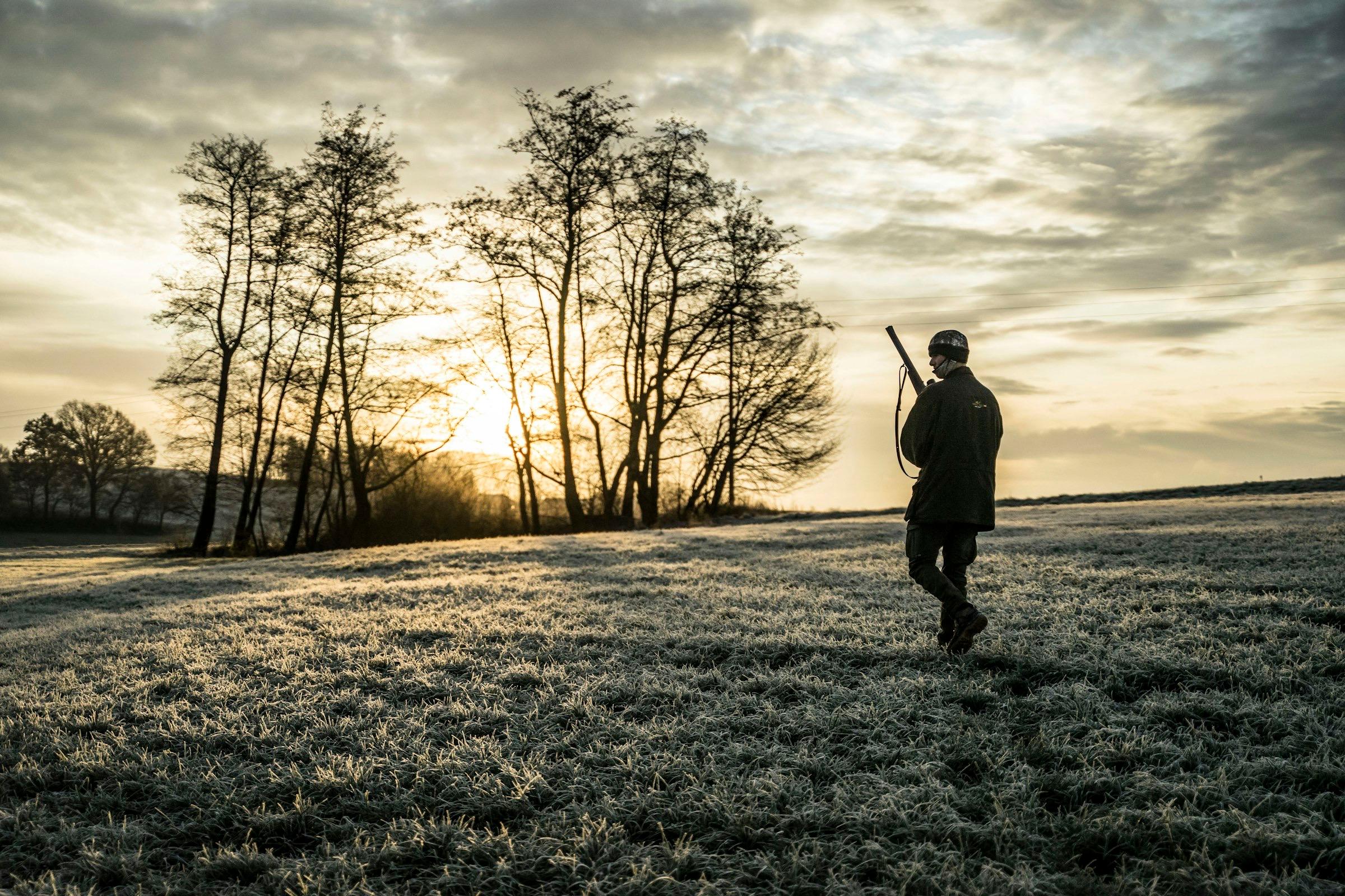 A hunter walking across a frosted field toward the tree line at sunrise.