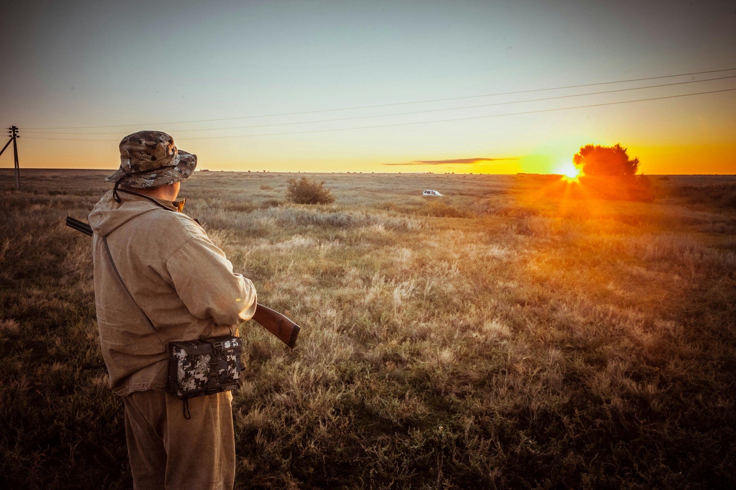 A hunter in a field of tall grass, watching the sun go down.